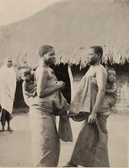 A group of women standing in front of a thatched-roof building