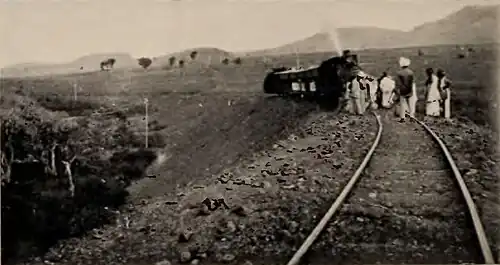 A train line with several persons standing on the tracks in front of a train