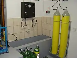 A small stationary installation with Bauer Mariner II, filling panel, water bath and storage bank. (the storage cylinders were spares intended for a diving bell and would not normally be yellow and grey)