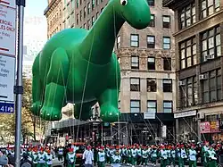 Many people carry along a balloon in the shape of a green dinosaur