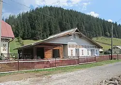 A wide white house with folk motifs painted along the middle of it in a rural location.