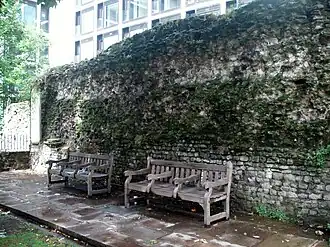 Photograph of park benchs placed against a section of the London Wall in a public city garden.