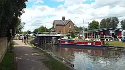 A picturesque river scene, with a deep-red canal boat in the centre and a black and white lock in the background.