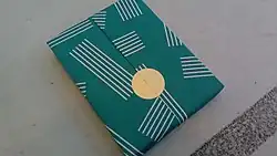 A book, already wrapped, with a large, flat, gold sticker or seal instead of a three-dimensional bow